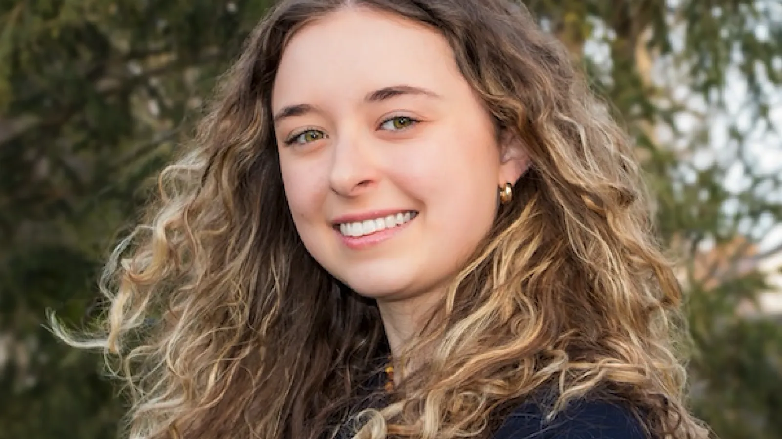 young woman smiling with trees in the background